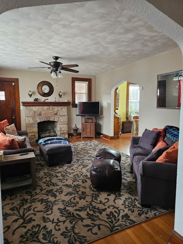 living room with ceiling fan, a textured ceiling, light wood-type flooring, and a fireplace