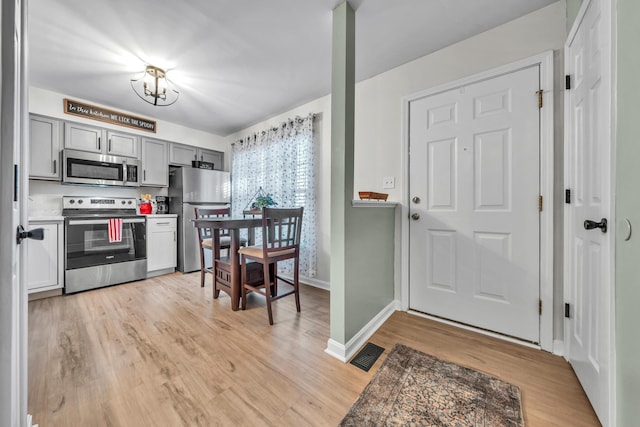 kitchen with stainless steel appliances, gray cabinetry, and light hardwood / wood-style flooring