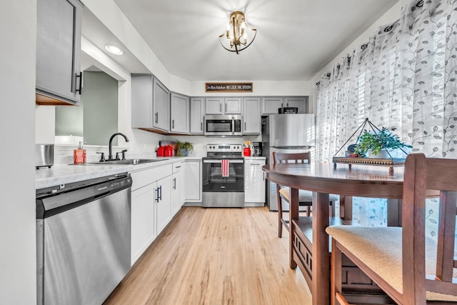 kitchen featuring appliances with stainless steel finishes, sink, gray cabinets, and light hardwood / wood-style flooring