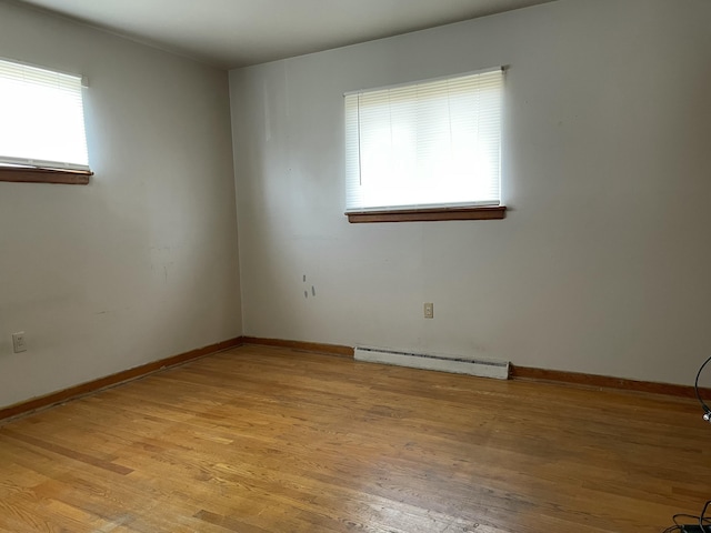 spare room featuring baseboard heating, a wealth of natural light, and light hardwood / wood-style flooring