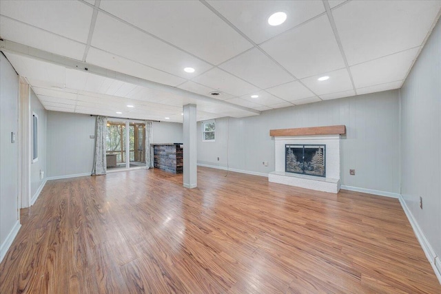 unfurnished living room featuring a brick fireplace, a drop ceiling, and hardwood / wood-style flooring