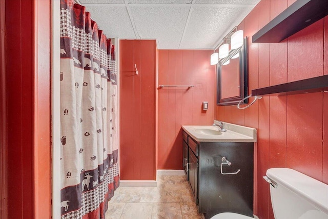 bathroom featuring toilet, a drop ceiling, wooden walls, and vanity