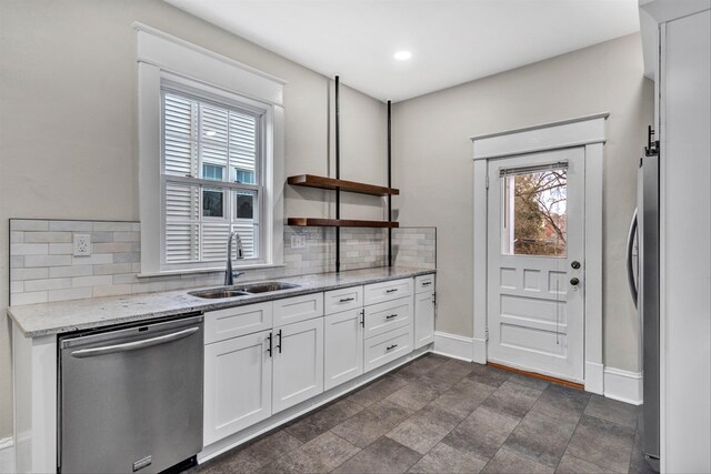 kitchen with sink, white cabinetry, stainless steel appliances, light stone countertops, and decorative backsplash