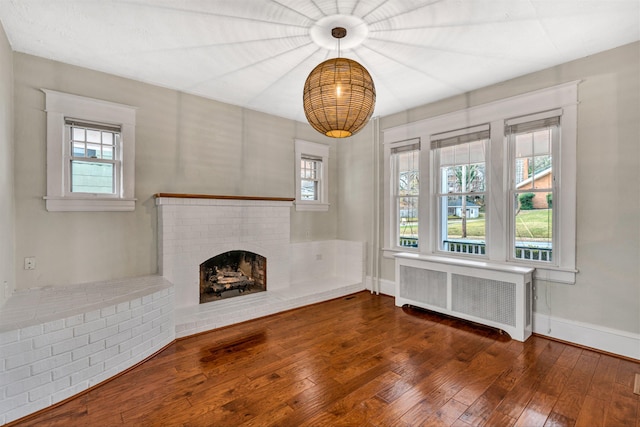 unfurnished living room featuring a healthy amount of sunlight, radiator, dark hardwood / wood-style floors, and a brick fireplace