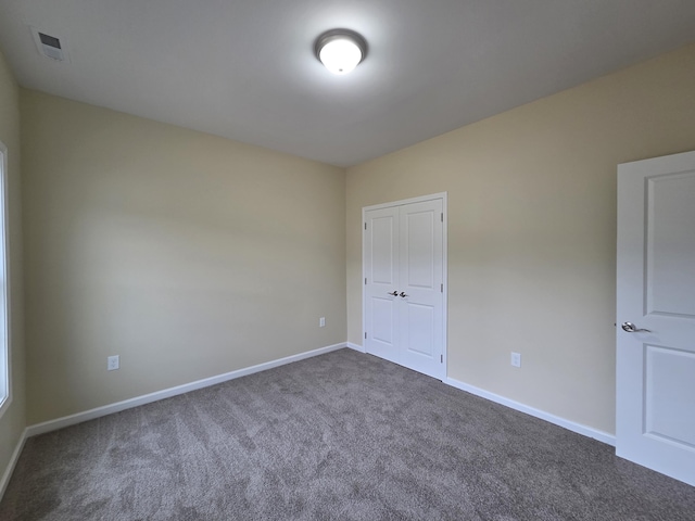 spare room featuring baseboards, dark colored carpet, and visible vents