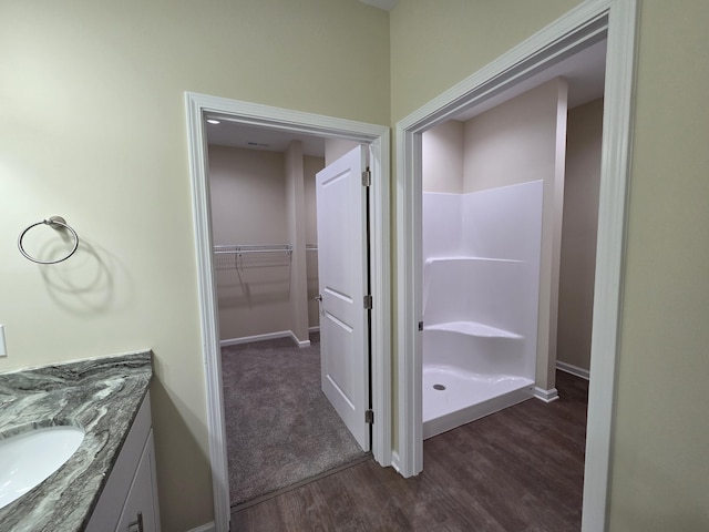 full bath featuring walk in shower, wood finished floors, vanity, and baseboards