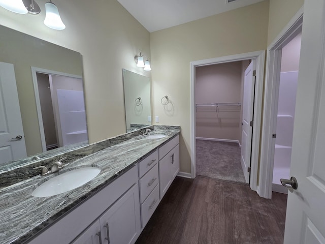 bathroom with a walk in closet, double vanity, a sink, and wood finished floors