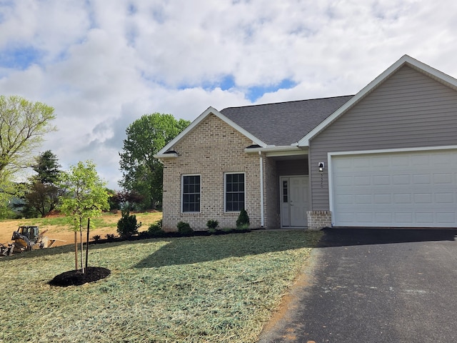 single story home featuring driveway, a shingled roof, a front yard, brick siding, and a garage