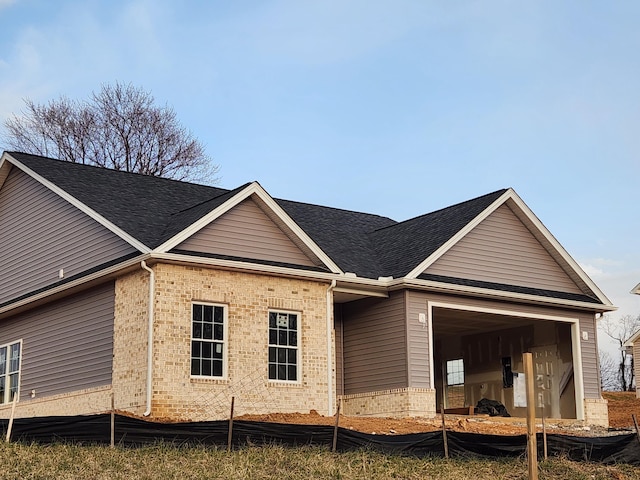 exterior space with brick siding, an attached garage, and roof with shingles