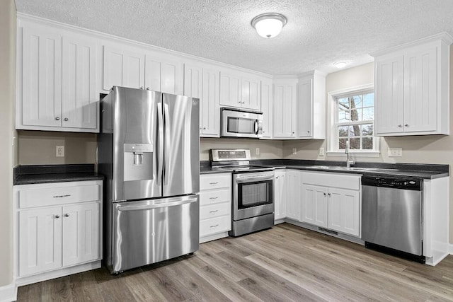 kitchen featuring white cabinets, appliances with stainless steel finishes, sink, and light wood-type flooring