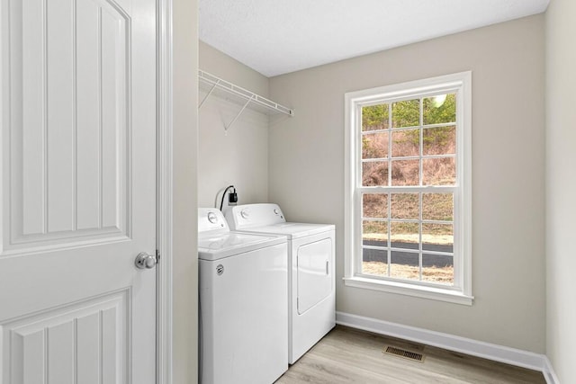 laundry room with a wealth of natural light, washing machine and clothes dryer, and light hardwood / wood-style floors