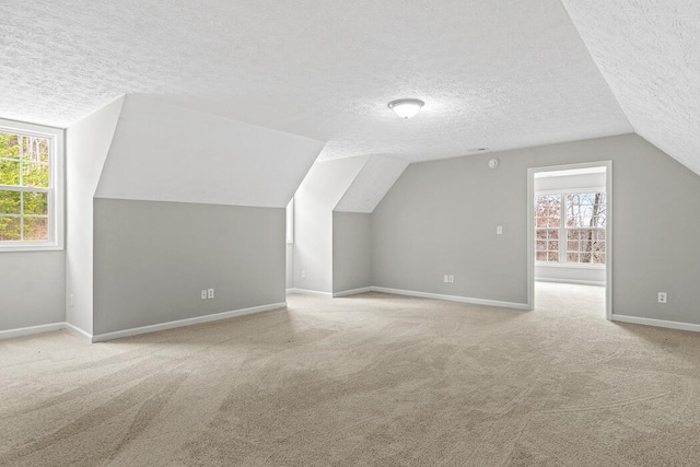 additional living space with plenty of natural light, a textured ceiling, light carpet, and vaulted ceiling