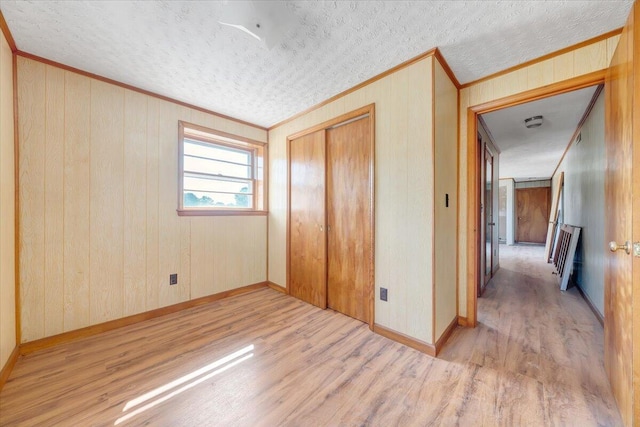 unfurnished bedroom with a closet, wood walls, ornamental molding, and light hardwood / wood-style floors