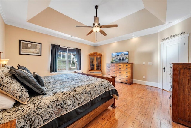 bedroom with baseboards, light wood-style flooring, ceiling fan, ornamental molding, and a tray ceiling