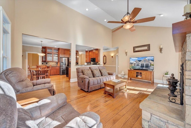 living area with light wood-type flooring, baseboards, high vaulted ceiling, and a stone fireplace