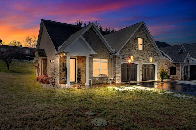 exterior space featuring driveway, a garage, stone siding, a yard, and brick siding