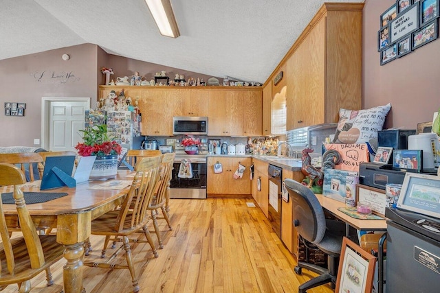 kitchen featuring appliances with stainless steel finishes, lofted ceiling, light hardwood / wood-style floors, sink, and backsplash