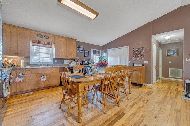 dining area featuring sink, a textured ceiling, vaulted ceiling, and light wood-type flooring