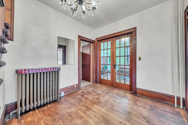 empty room featuring french doors, a chandelier, and wood-type flooring