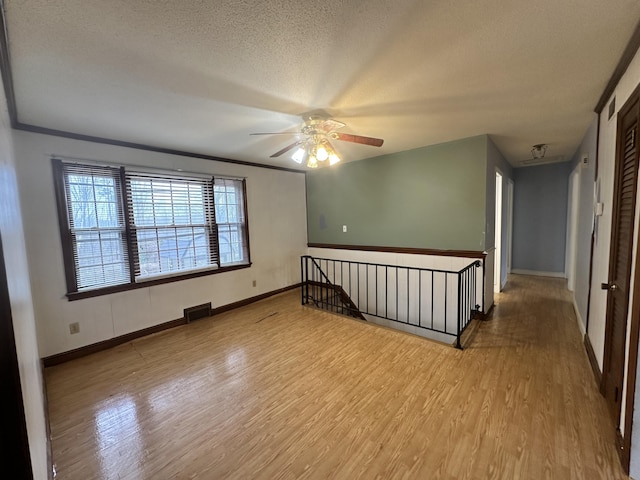 empty room featuring a textured ceiling, ceiling fan, crown molding, and light hardwood / wood-style floors