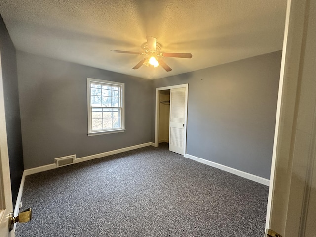 unfurnished bedroom featuring ceiling fan, a textured ceiling, a closet, and dark colored carpet