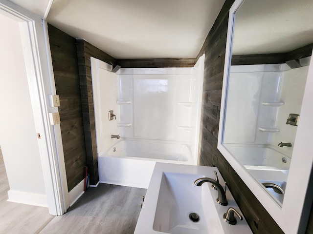 bathroom with shower / washtub combination, wood walls, and wood finished floors