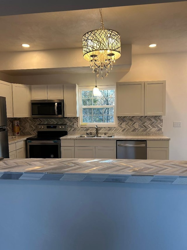 kitchen featuring white cabinetry, appliances with stainless steel finishes, backsplash, a notable chandelier, and sink