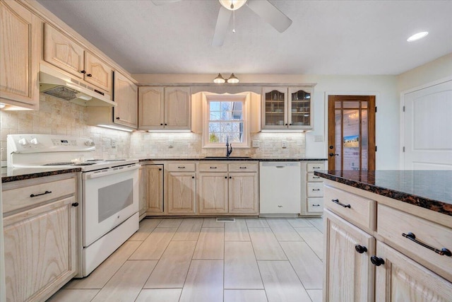 kitchen with sink, dark stone counters, white appliances, and light brown cabinets