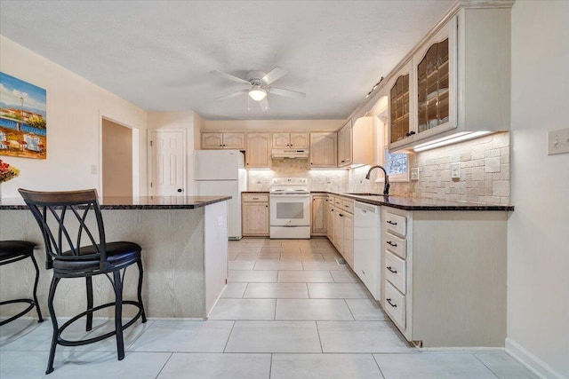 kitchen with sink, white appliances, kitchen peninsula, and dark stone counters