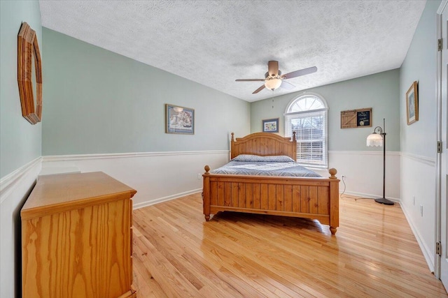 bedroom with light wood-type flooring, ceiling fan, and a textured ceiling