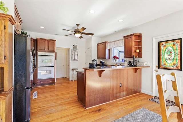 kitchen with stainless steel fridge, white double oven, a kitchen breakfast bar, kitchen peninsula, and light wood-type flooring