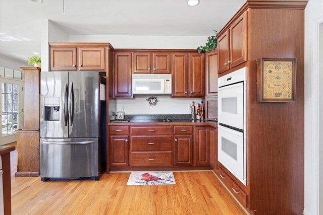 kitchen with white appliances, dark stone counters, and light hardwood / wood-style flooring