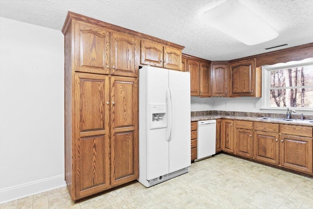 kitchen with visible vents, brown cabinetry, a sink, a textured ceiling, and white fridge with ice dispenser