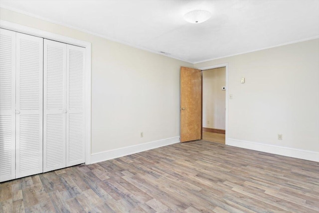 unfurnished bedroom featuring crown molding, light hardwood / wood-style floors, and a closet