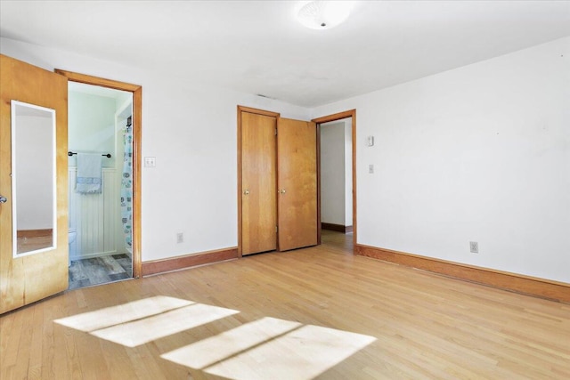 unfurnished bedroom with ensuite bath, light wood-style flooring, and baseboards