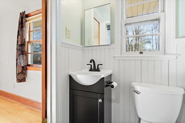 bathroom with toilet, vanity, wood finished floors, and wainscoting