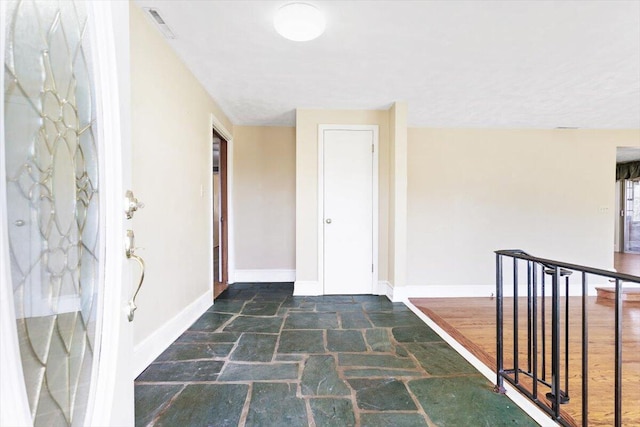 hall featuring visible vents, baseboards, and stone tile flooring