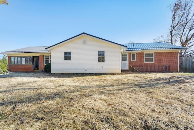 back of property featuring a sunroom, brick siding, and metal roof