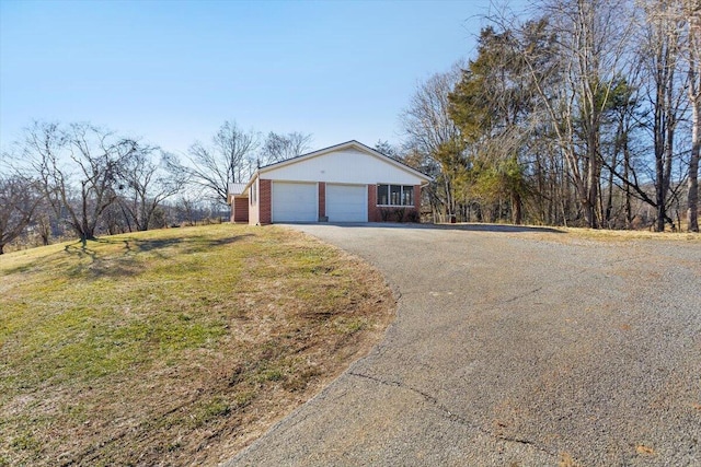 exterior space with driveway, a yard, an attached garage, and brick siding