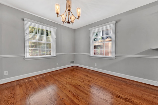 spare room with an inviting chandelier and hardwood / wood-style flooring