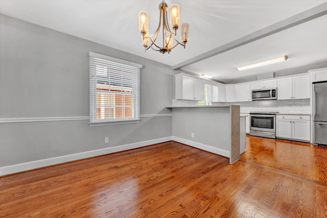 kitchen featuring white cabinetry, tasteful backsplash, hanging light fixtures, light hardwood / wood-style flooring, and stainless steel appliances