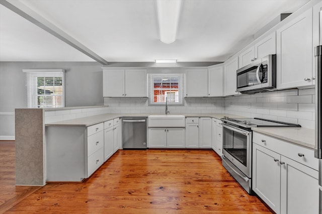 kitchen featuring sink, tasteful backsplash, kitchen peninsula, stainless steel appliances, and white cabinets