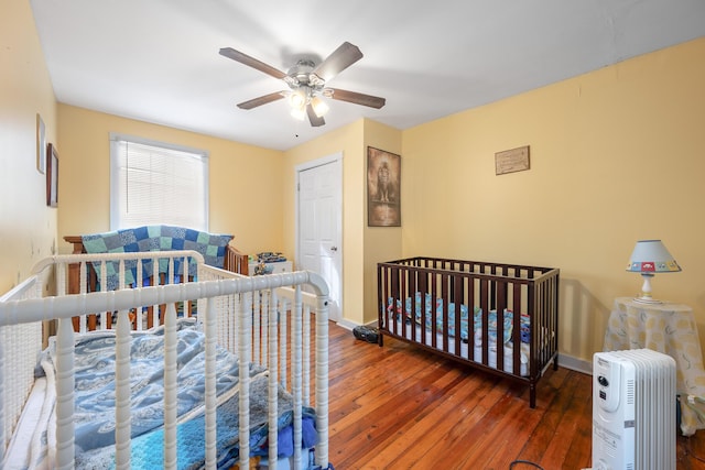 bedroom featuring ceiling fan, dark wood-type flooring, and a crib