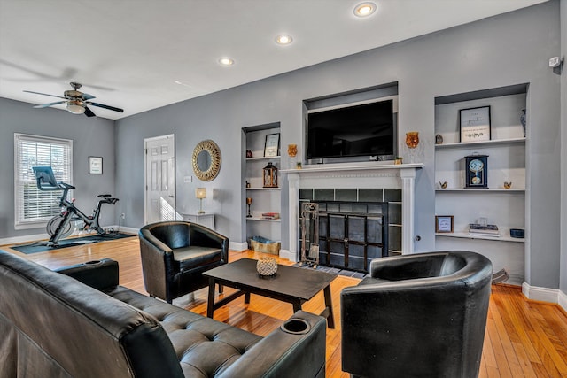 living room with built in features, ceiling fan, light hardwood / wood-style flooring, and a tiled fireplace