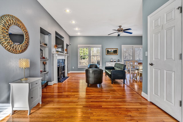 living room featuring built in shelves, light hardwood / wood-style flooring, and ceiling fan