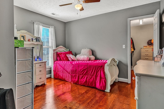 bedroom with a textured ceiling, ceiling fan, and dark hardwood / wood-style flooring