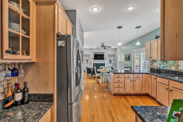 kitchen with decorative light fixtures, tasteful backsplash, dark stone countertops, stainless steel fridge with ice dispenser, and light hardwood / wood-style flooring