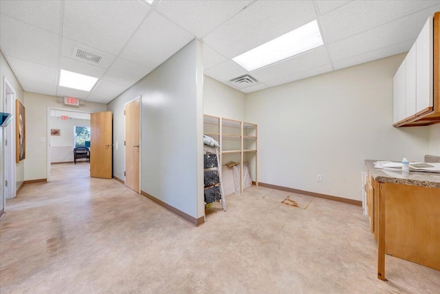 interior space featuring light colored carpet, a drop ceiling, and white cabinets