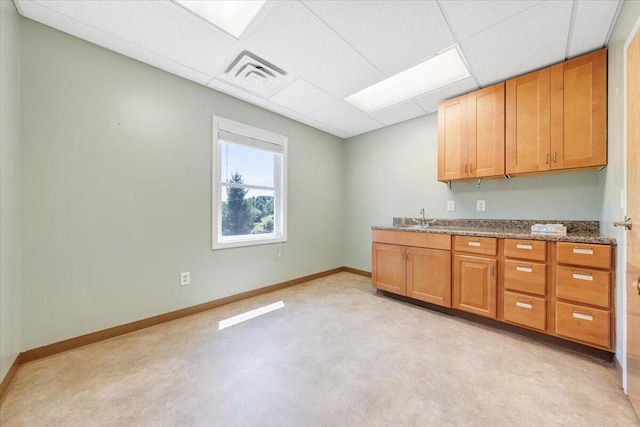 kitchen with stone counters, a drop ceiling, and sink