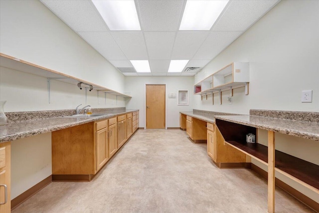 kitchen featuring built in desk, sink, light stone counters, light colored carpet, and a drop ceiling